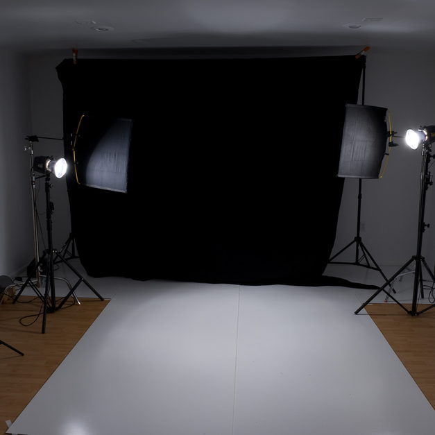 A black backdrop hung above a white studio floor, lit from both sides by softboxes on stands.