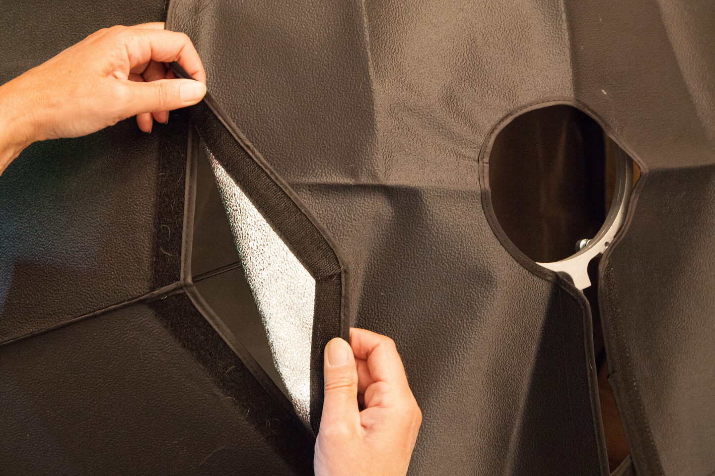Two hands fitting the black outer skin of an octagonal softbox over its silver lining.