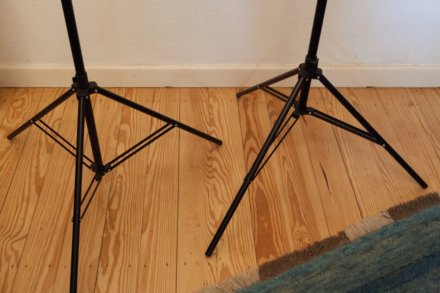 Two black lighting stands with their legs splayed on a bare wooden studio floor.