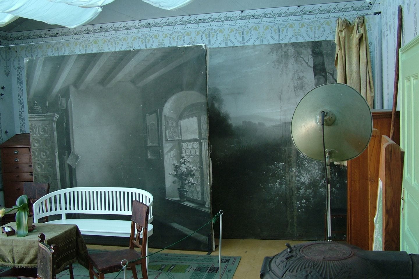 Large painted scenic backdrops and a reflector dish on a stand in a preserved portrait atelier.