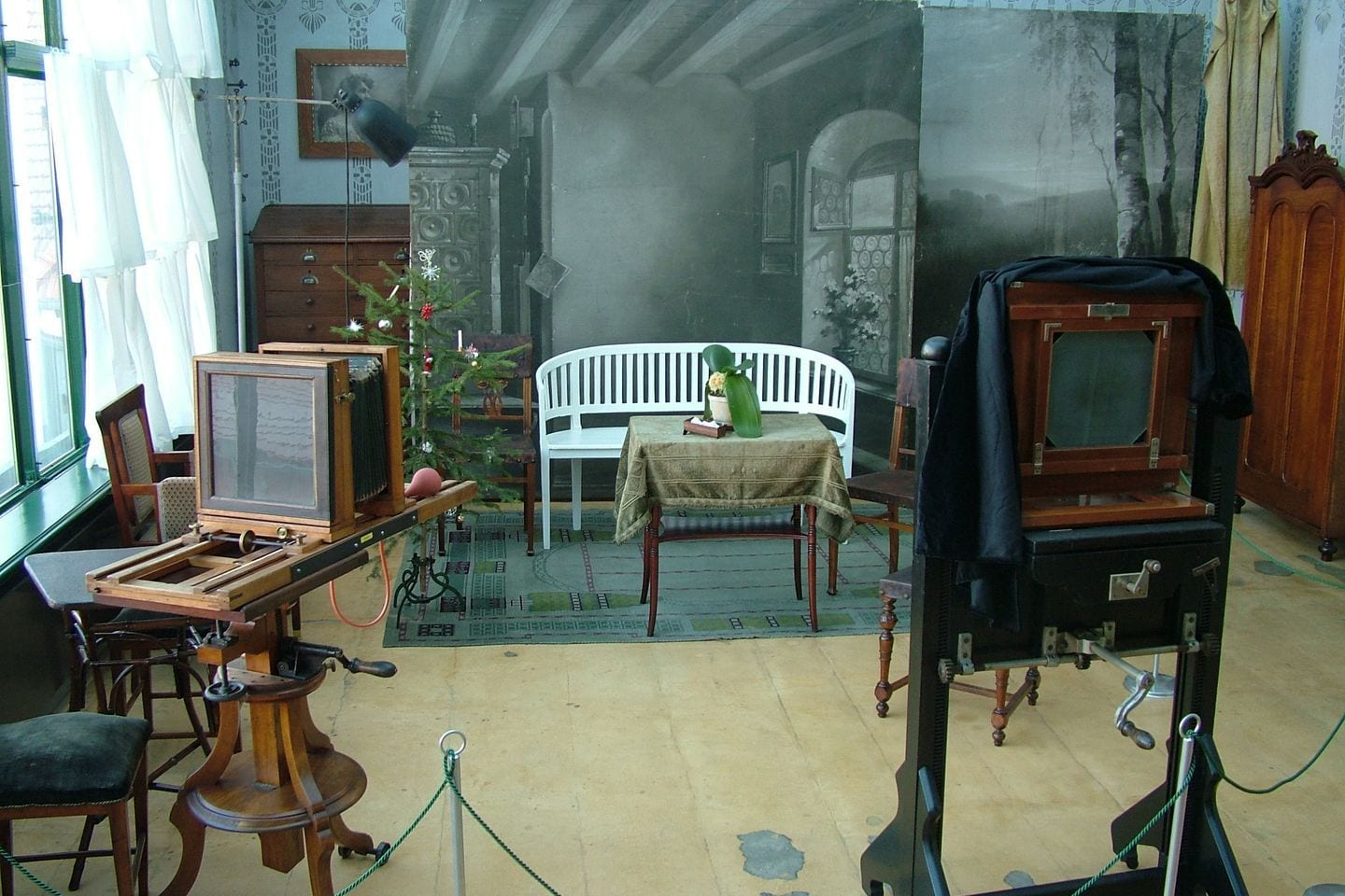 Two wooden plate cameras facing a white bench and a set table in a preserved portrait atelier.