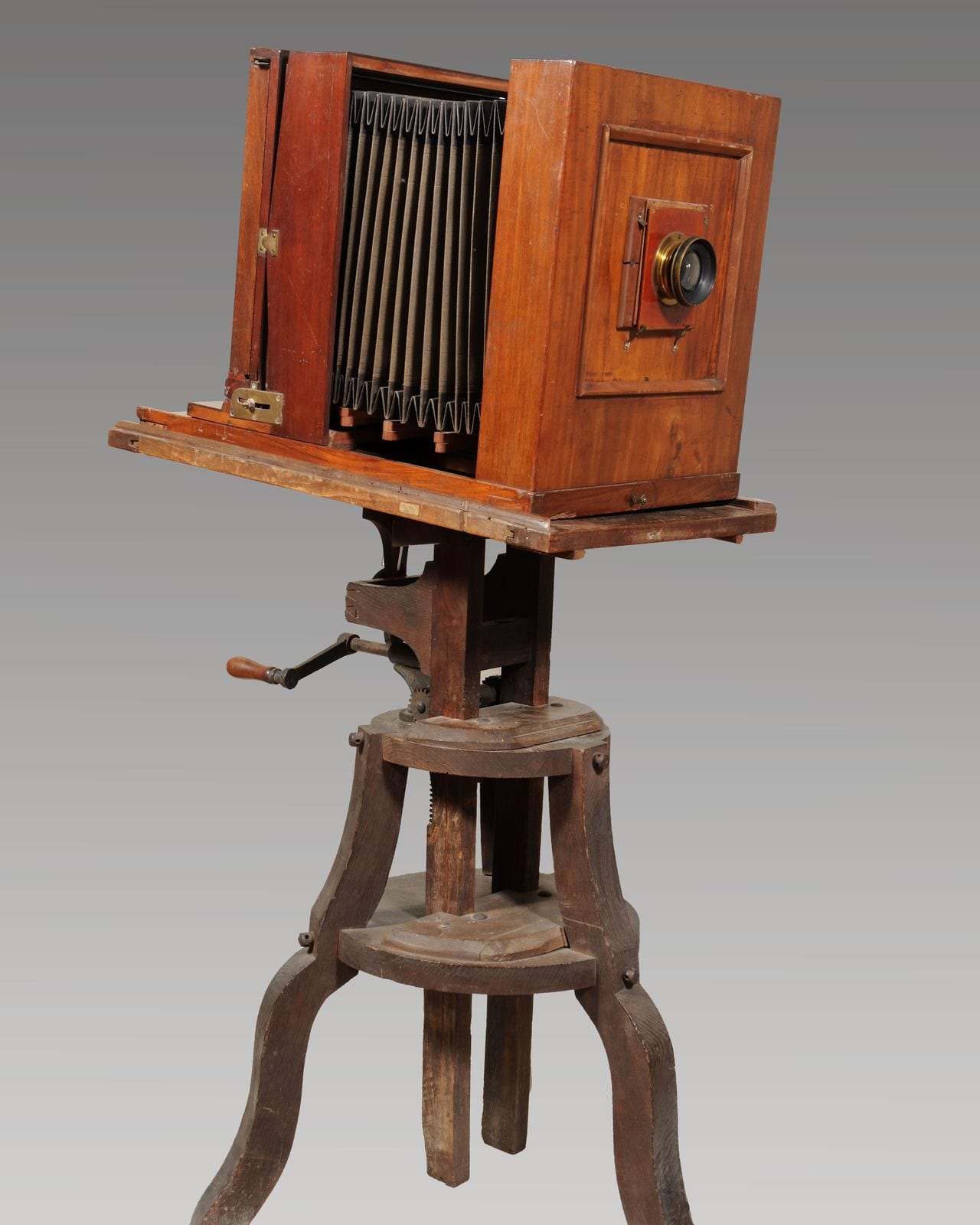 A wooden bellows camera mounted on a turned wooden stand, photographed against a grey ground.