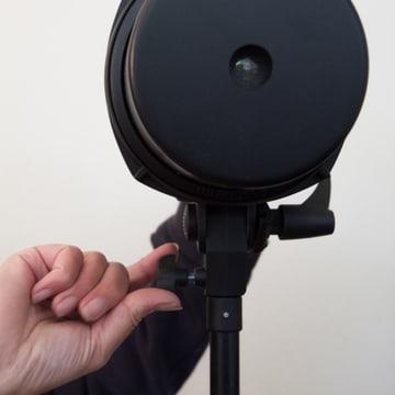 A beauty dish on a light stand, a hand on the tilt knob setting its angle