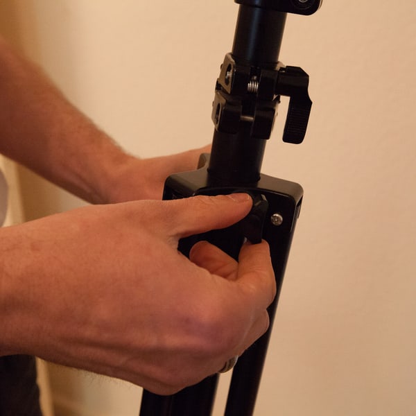 Both hands working the collar clamp on a light stand column