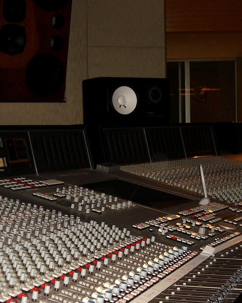 A long mixing console in perspective, with a studio monitor standing behind it.