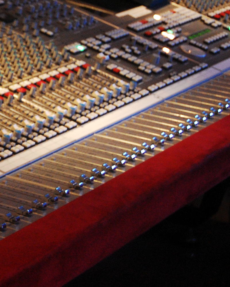 A run of mixing-console faders above a red leather armrest, photographed along their length.