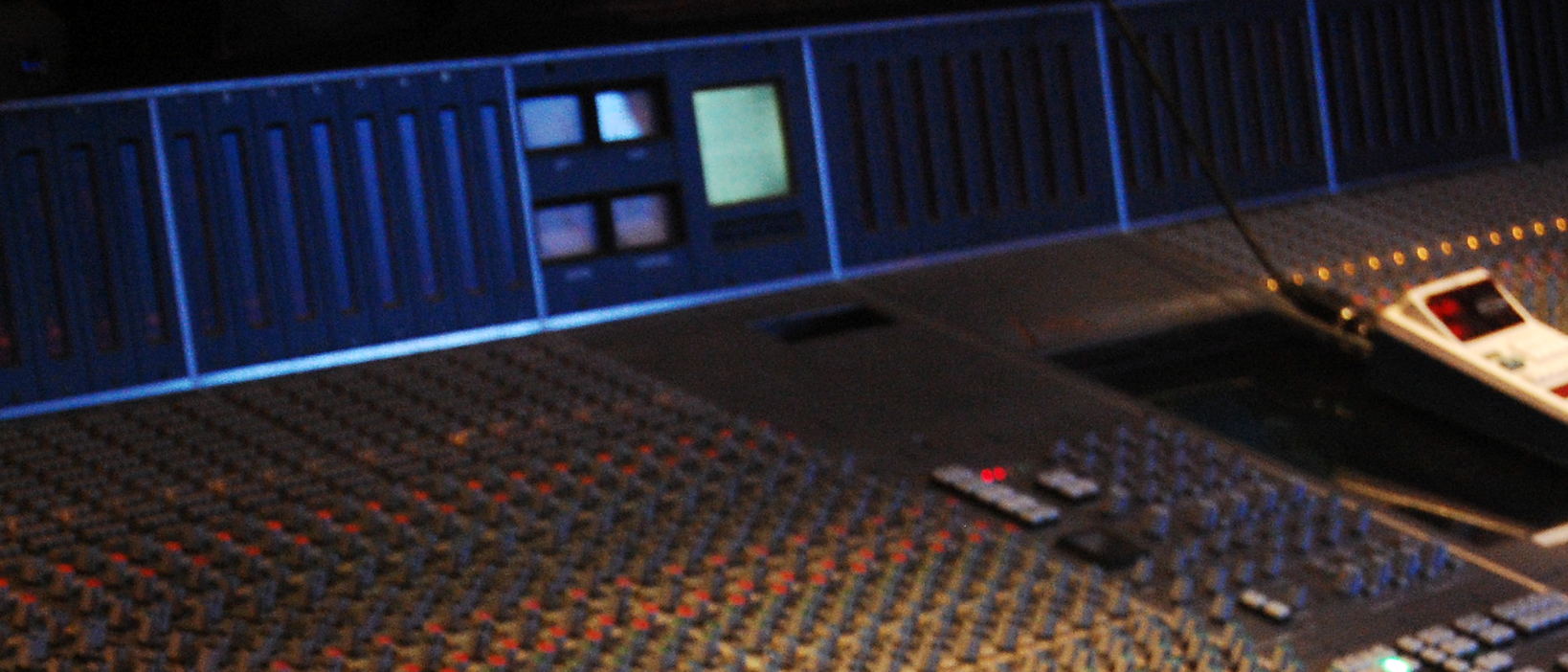 A console meter bridge glowing in blue light, with a desk remote in front of it in a dark room.