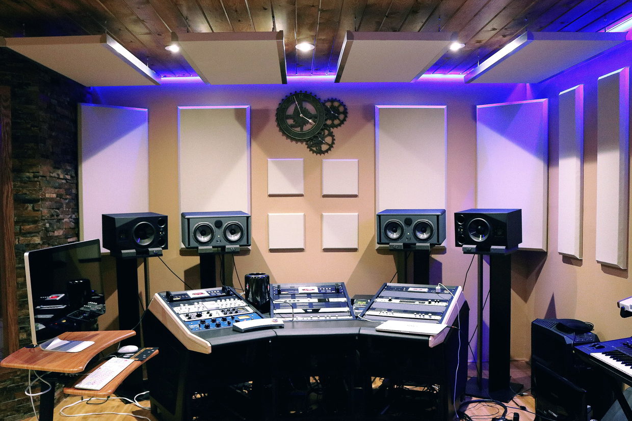 A control room lit in violet and blue, with a desk, monitors and racks and no one at the chair.
