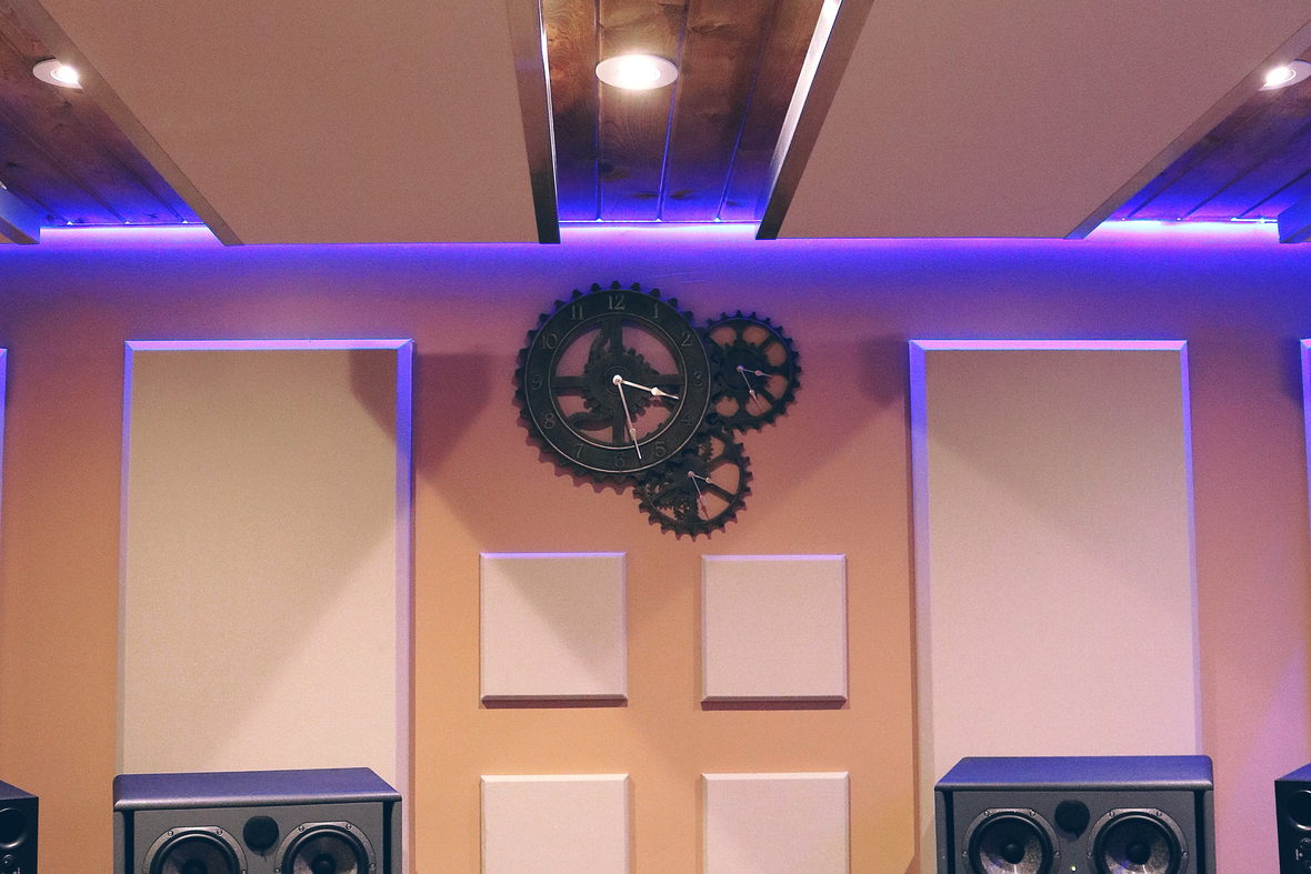 A tall wall of studio equipment lit from below in a narrow control room.
