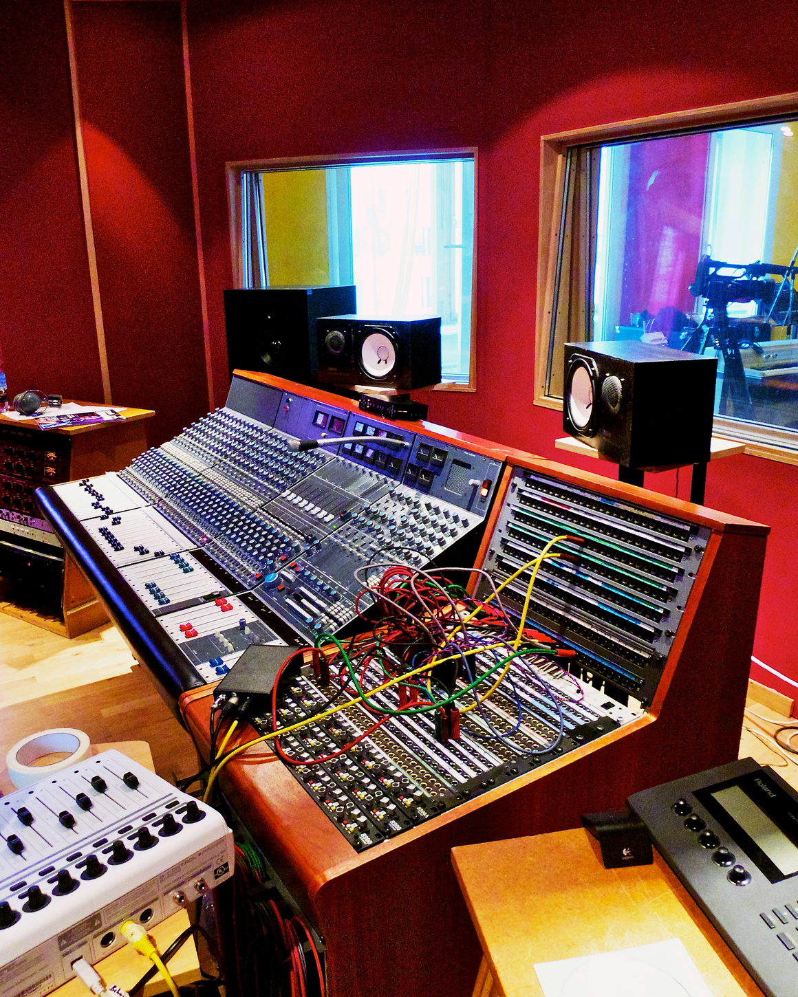 A control room in deep red light, with a large console and coloured patch cables.