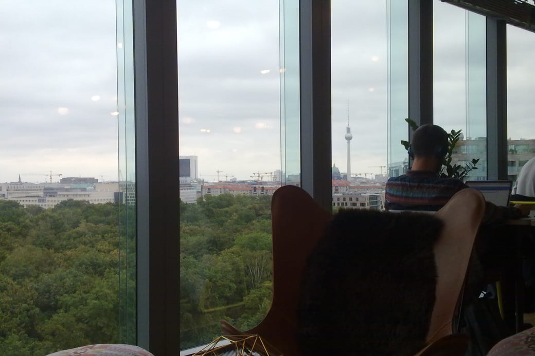A person seated in a lounge chair at a floor-to-ceiling window, looking out over a city skyline.
