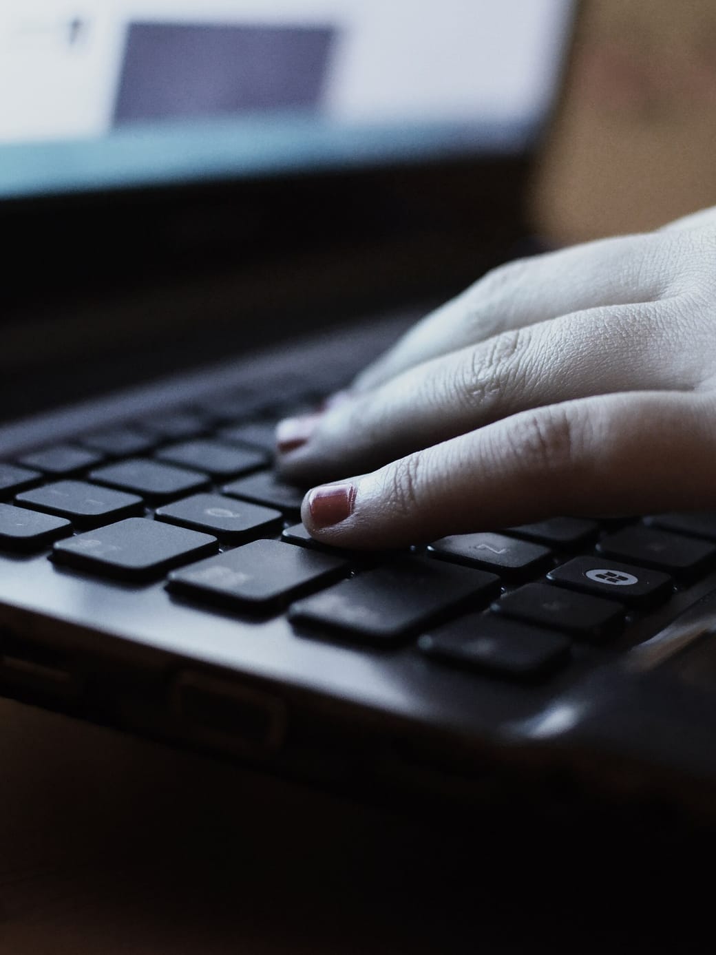 A hand resting on a laptop keyboard, photographed close in low, even light.