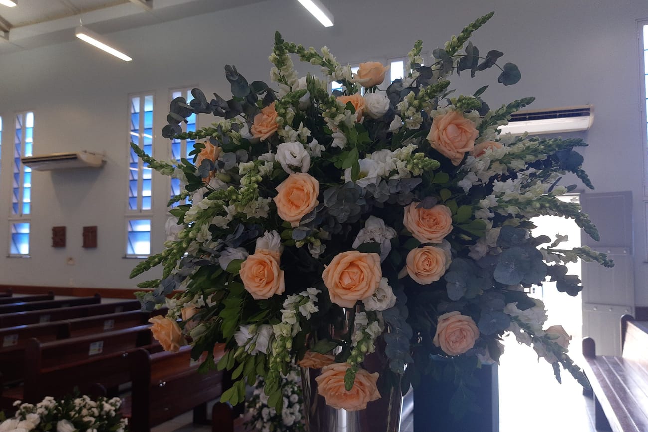 Tall pedestal arrangements of peach roses and snapdragons standing at the front of a church.