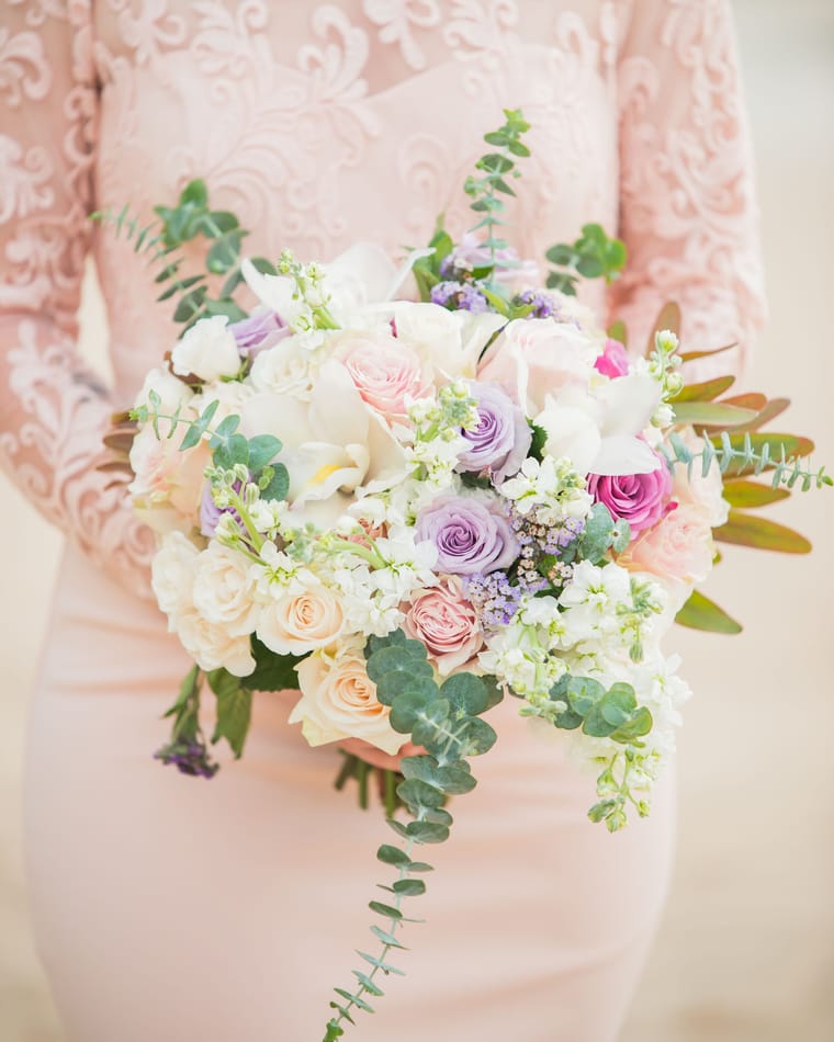 A loose blush bouquet of roses and foliage resting on pink lace.