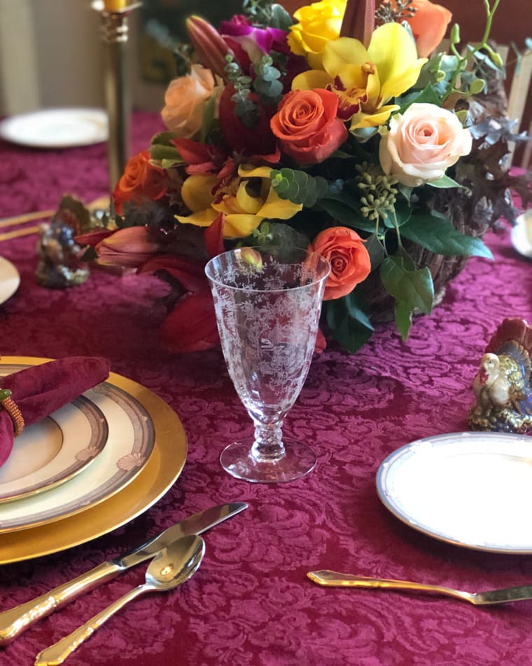 An autumn arrangement of orange roses and yellow orchids on a burgundy cloth.