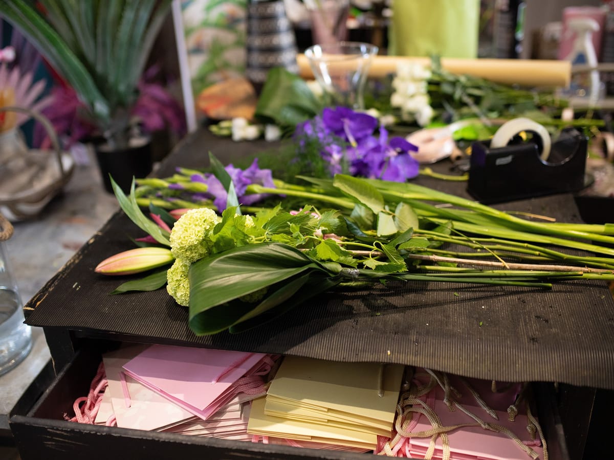 Cut orchids, foliage and trimmed stems laid out on a florist's workbench, photographed from directly above.