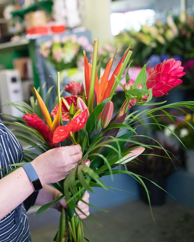A florist's hands holding a bright tropical bouquet in a flower shop. No face is visible.