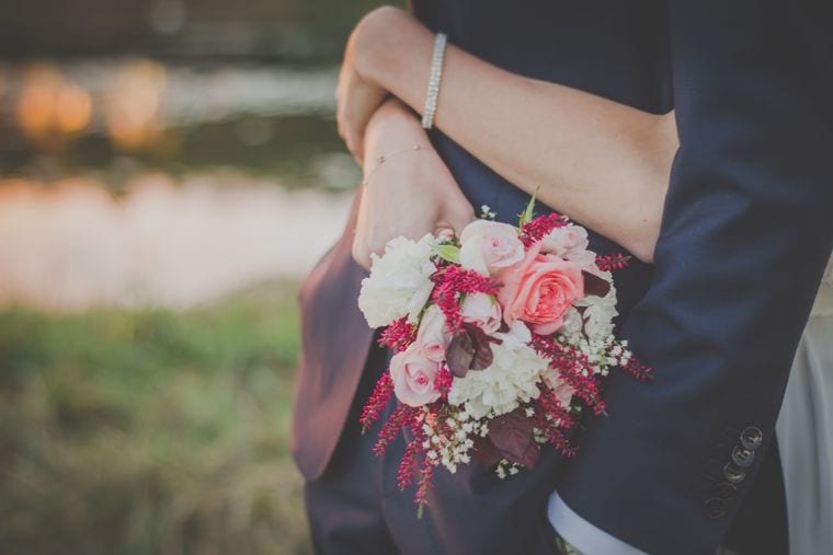 A bouquet of pink roses and red astilbe held between two people, both faces out of frame.