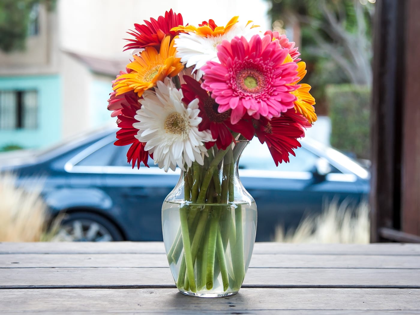 Red, pink, orange and white gerberas arranged in a clear glass vase on a wooden sill.