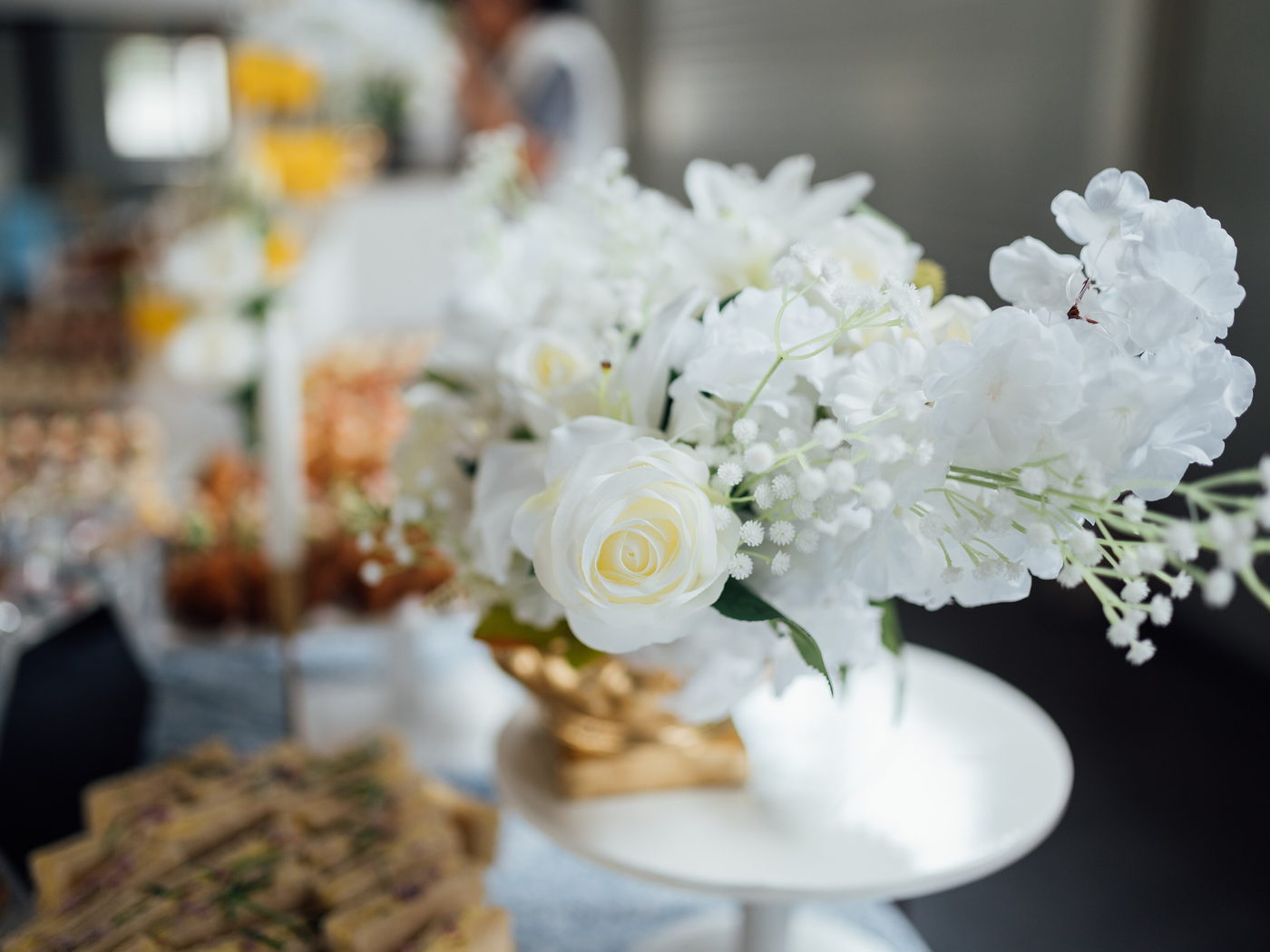 White roses, stock and gypsophila arranged in a footed vase.