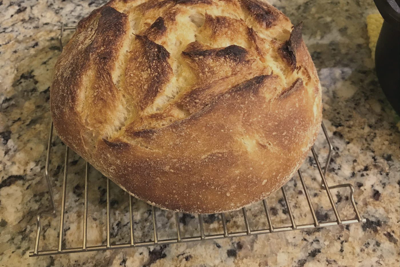 A round sourdough loaf cooling on a wire rack, its scored crust split open.