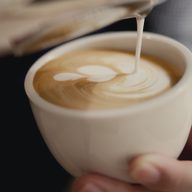 A white cup held in one hand taking the pour.