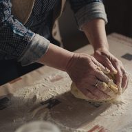 Floured hands folding dough on a bench.