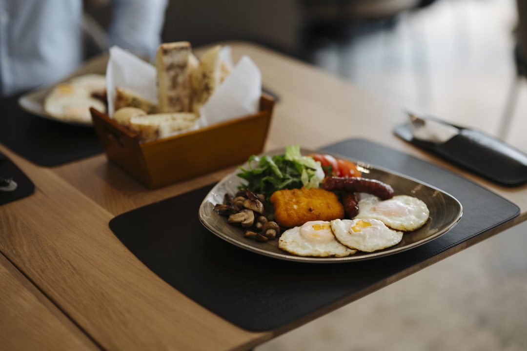 A breakfast plate of soft eggs, a grilled tomato half and a thick slice of toasted house loaf.