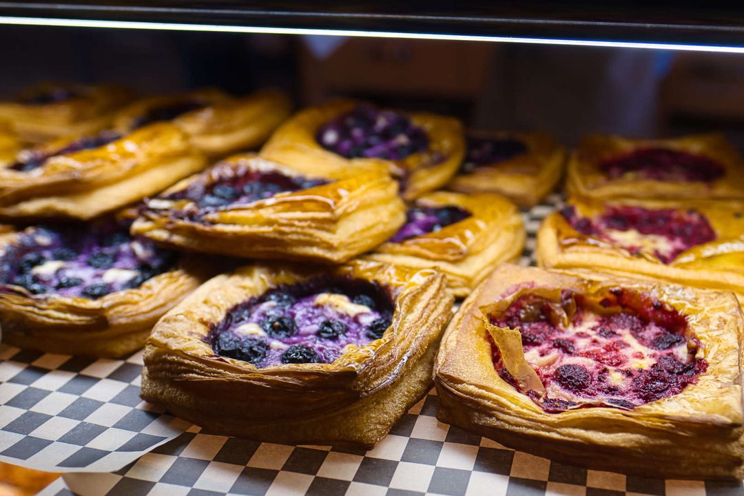 Rows of fruit-filled danish pastries on a checked tray inside a lit counter case.