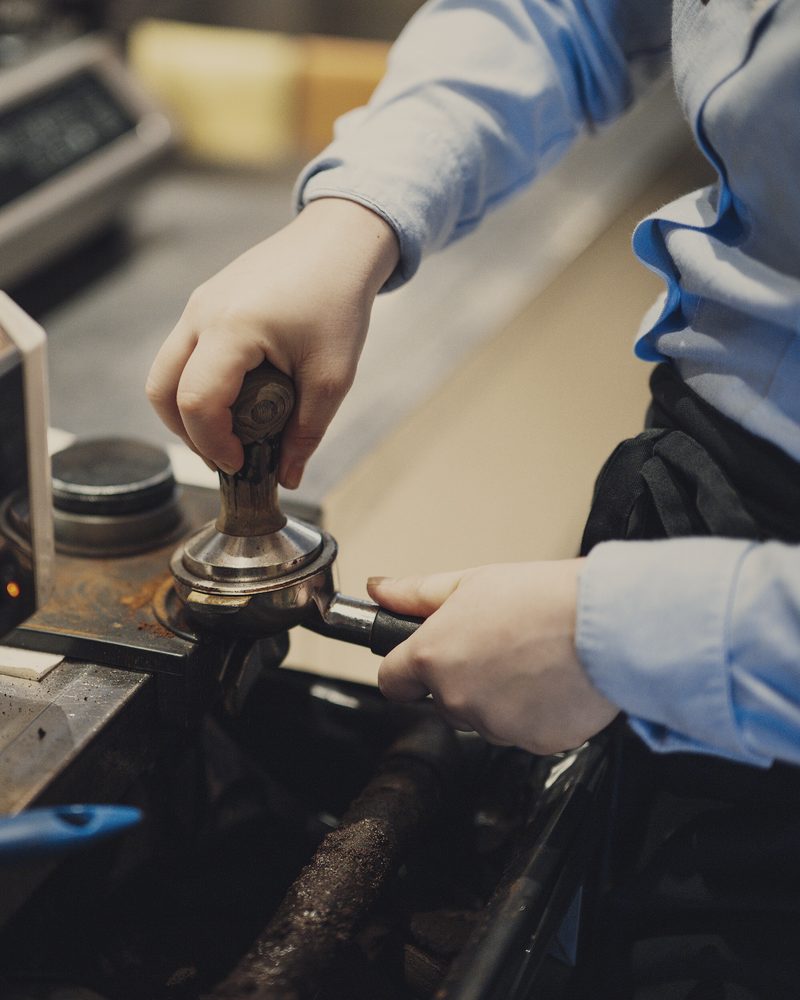 Two hands setting a loaded portafilter into the group head of an espresso machine behind the counter.