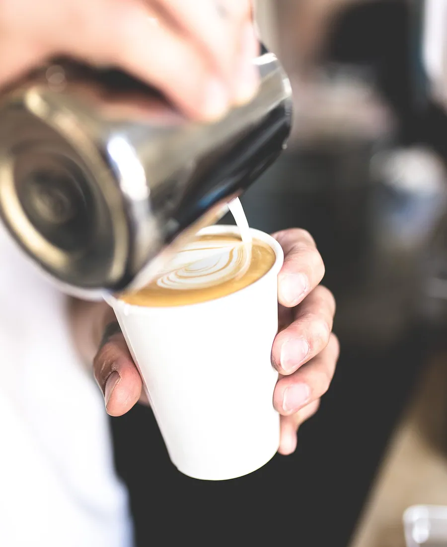 Hands pouring steamed milk into a coffee cup.