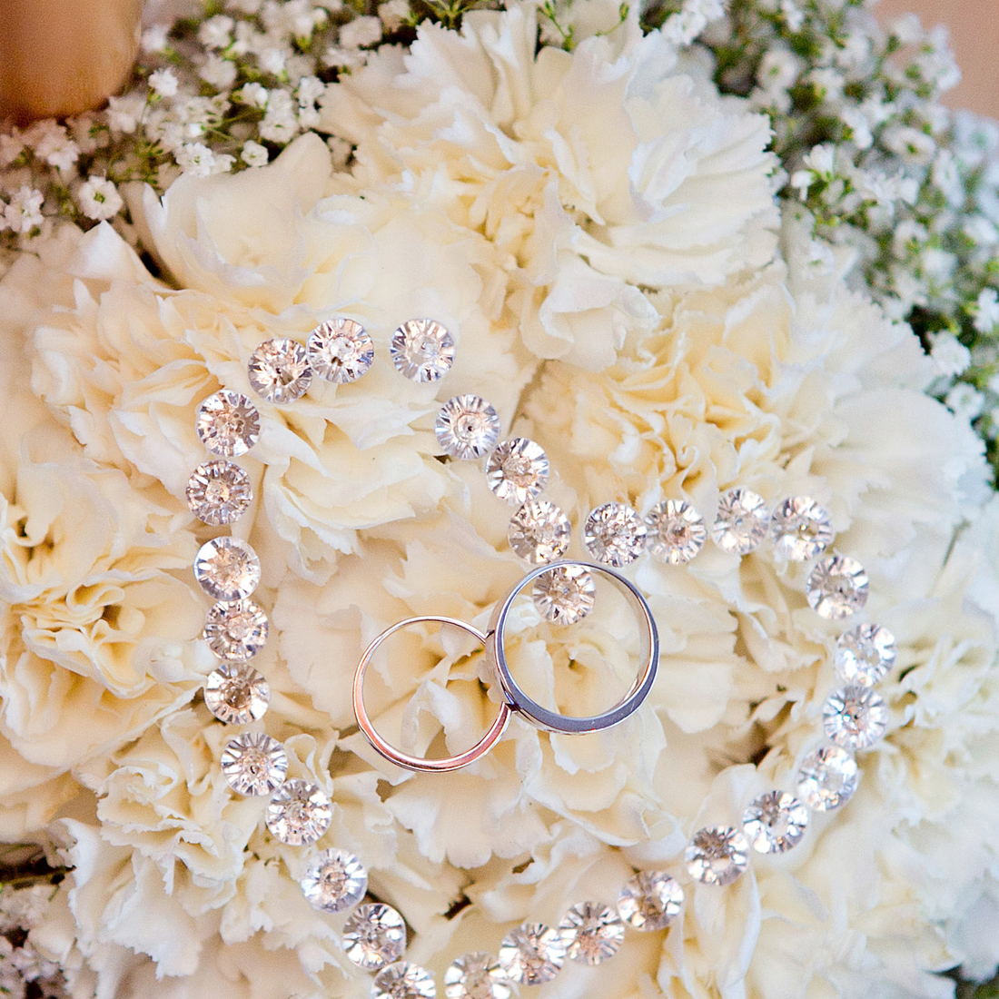 Two wedding bands, one rose gold and one white, resting on a bouquet of cream carnations.