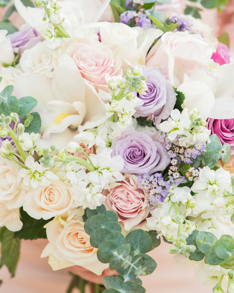 A close-packed bouquet of cream, peach and lilac roses with white stocks and eucalyptus.