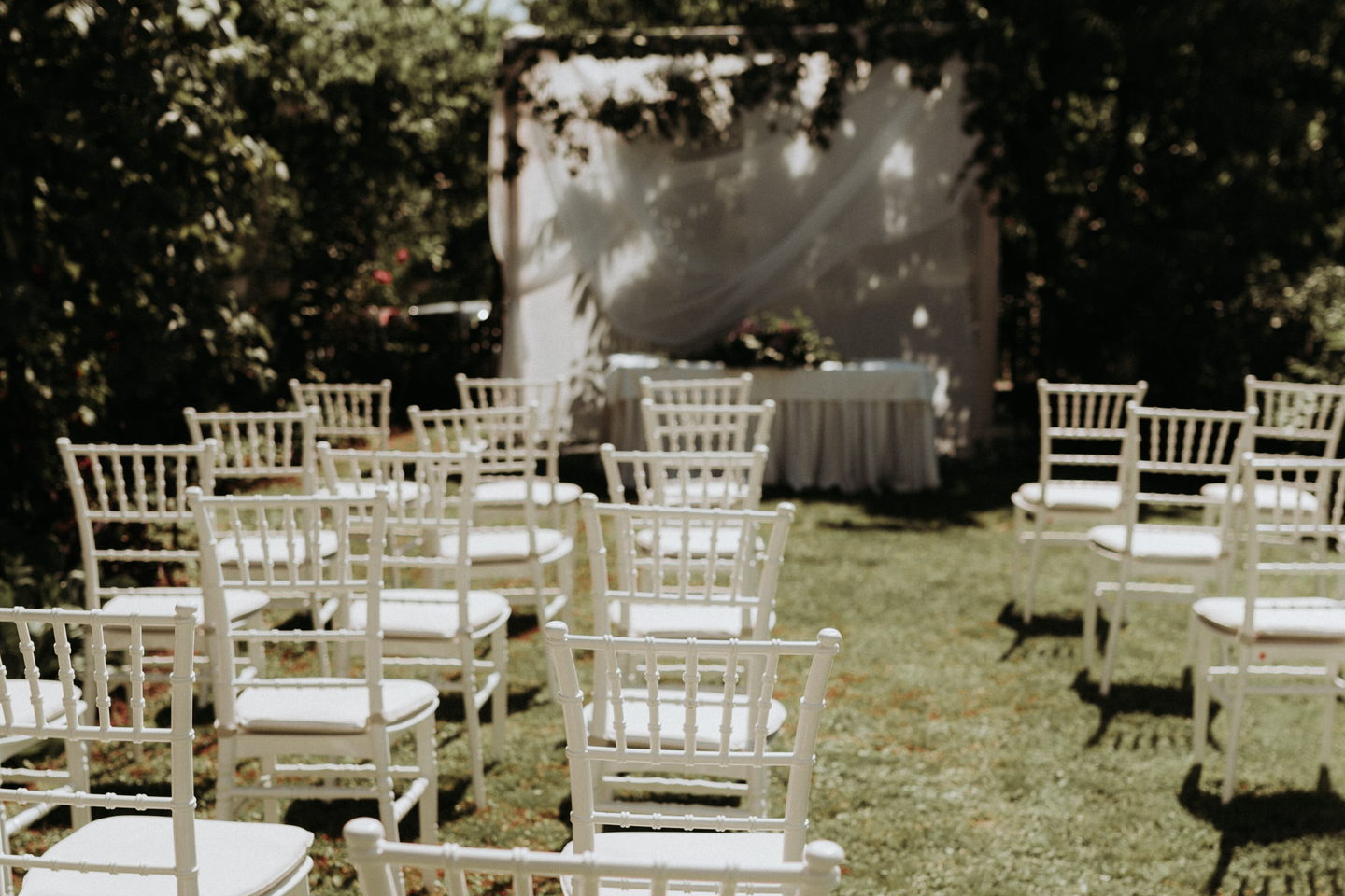 Rows of white chiavari chairs set out on a lawn facing a draped ceremony backdrop.