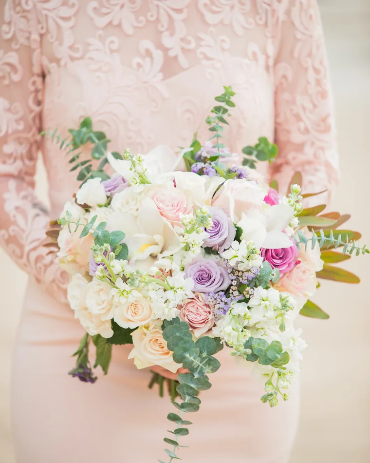 A bridal bouquet of pale roses and eucalyptus held against a blush dress.