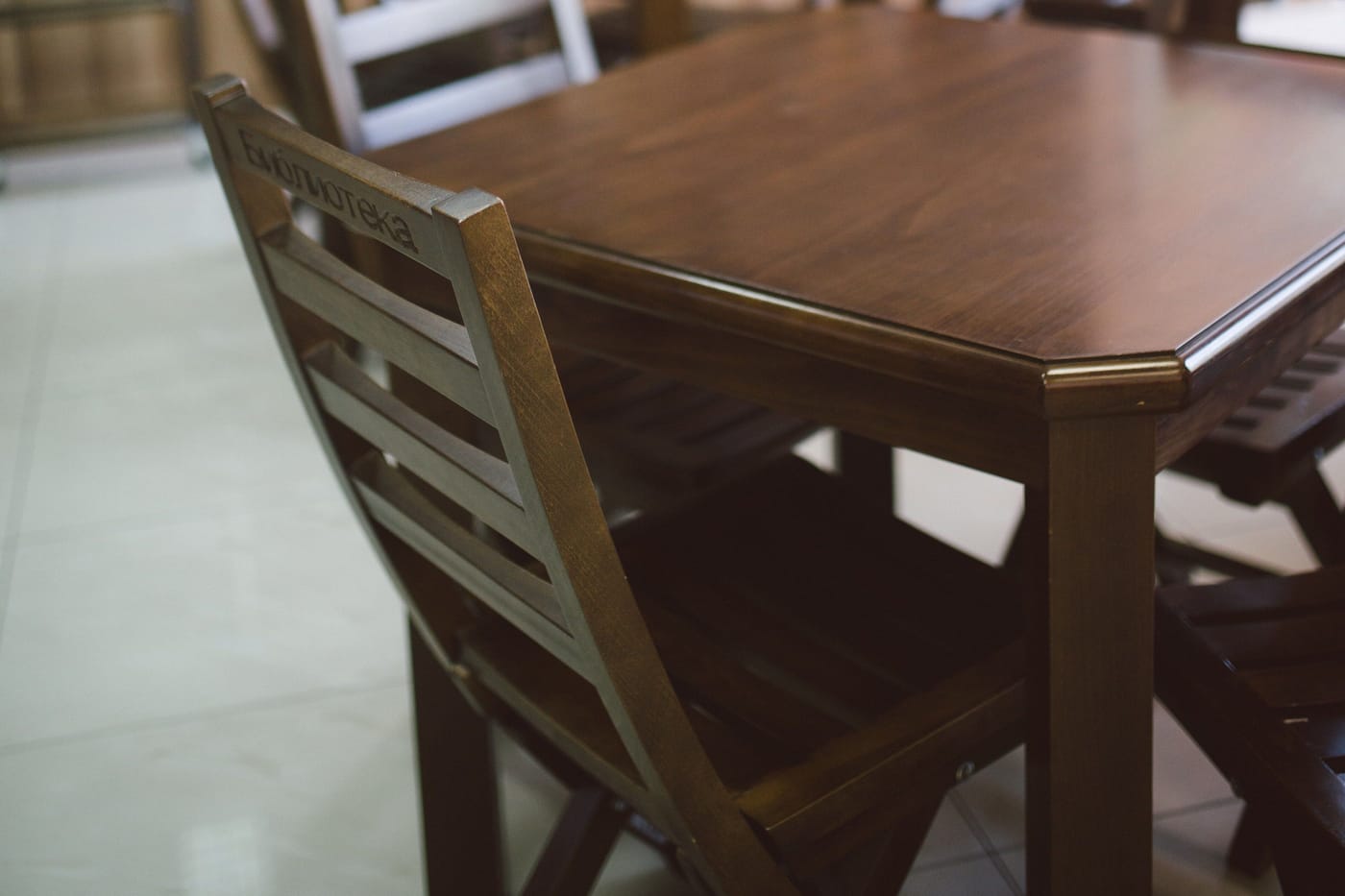 A dark wooden table and a slatted wooden chair on a pale tiled floor in a quiet reading room.