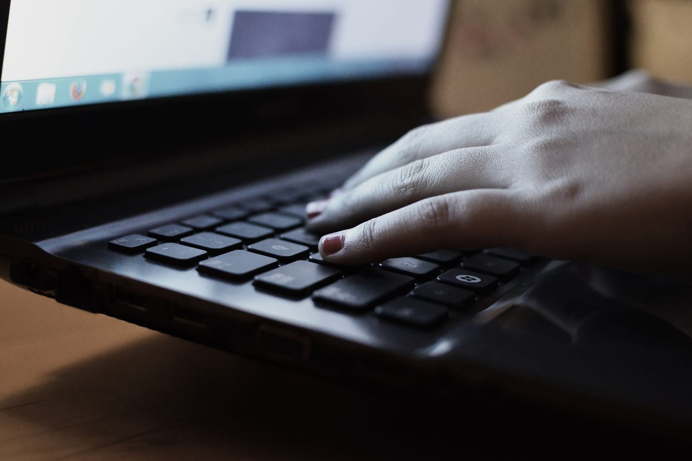 A hand resting on a laptop keyboard in low evening light, the edge of the screen visible at the top of the frame.