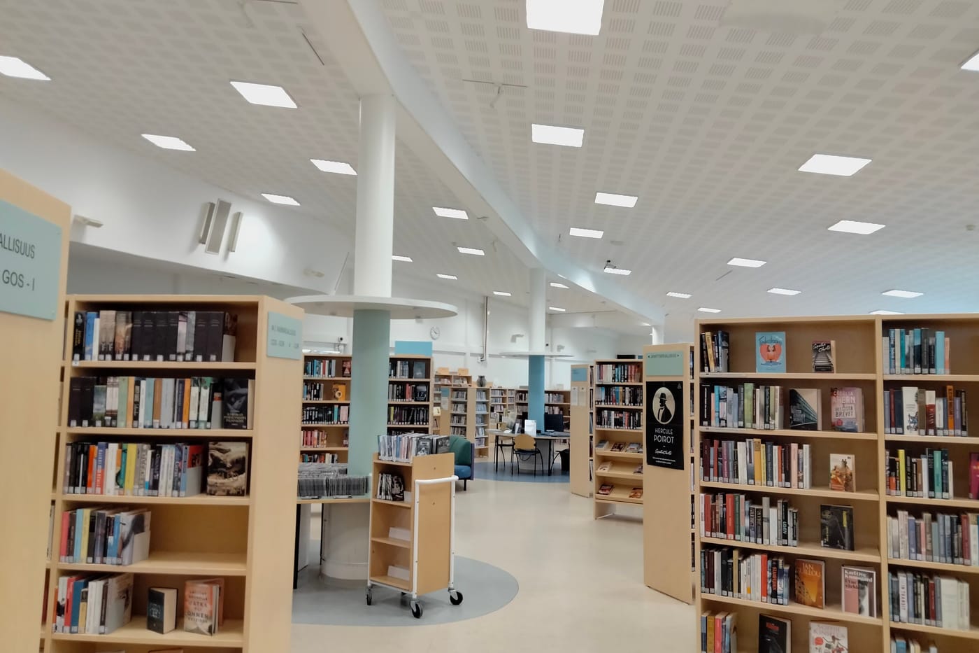 Rows of wooden bookshelves under a white panelled ceiling in a bright public library.