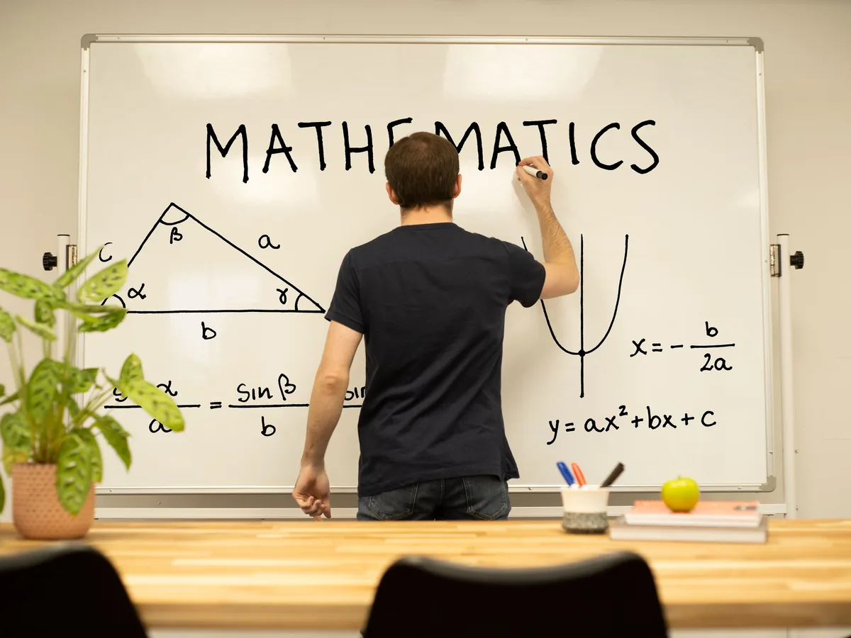 A tutor working a labelled triangle and quadratic formula on the whiteboard