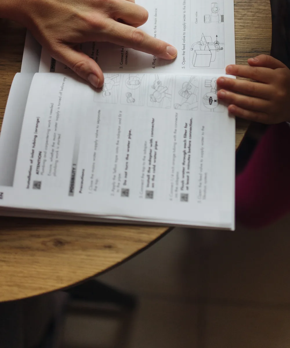 A tutor's hand points to the next step on the page while the student follows