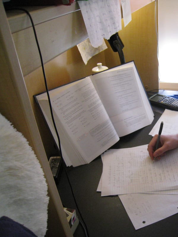 An open textbook on a stand, a calculator and pages of worked solutions