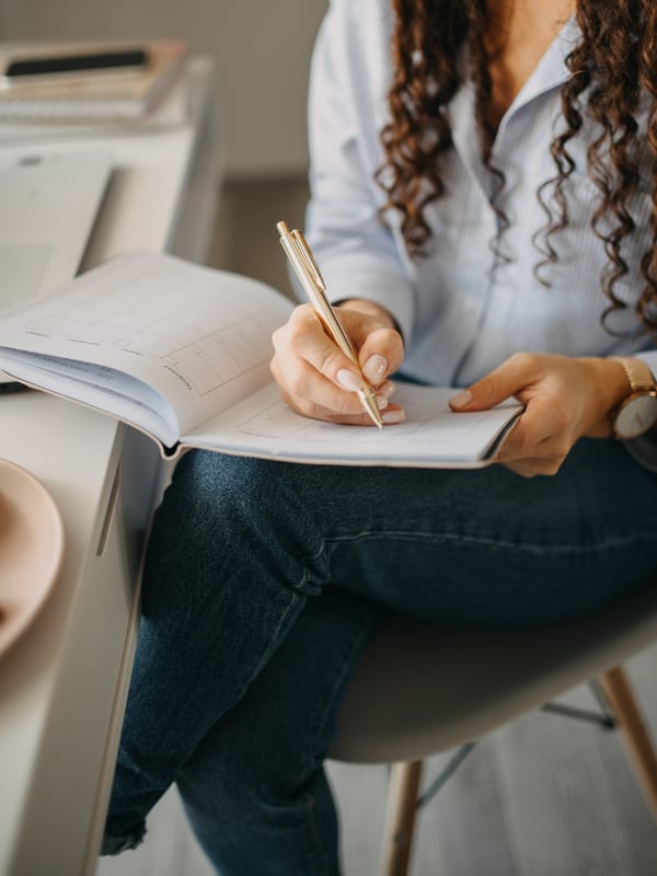 A student writing in a workbook at a desk, head out of frame
