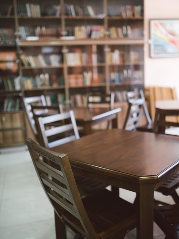 Wooden study tables between tall bookshelves in a library