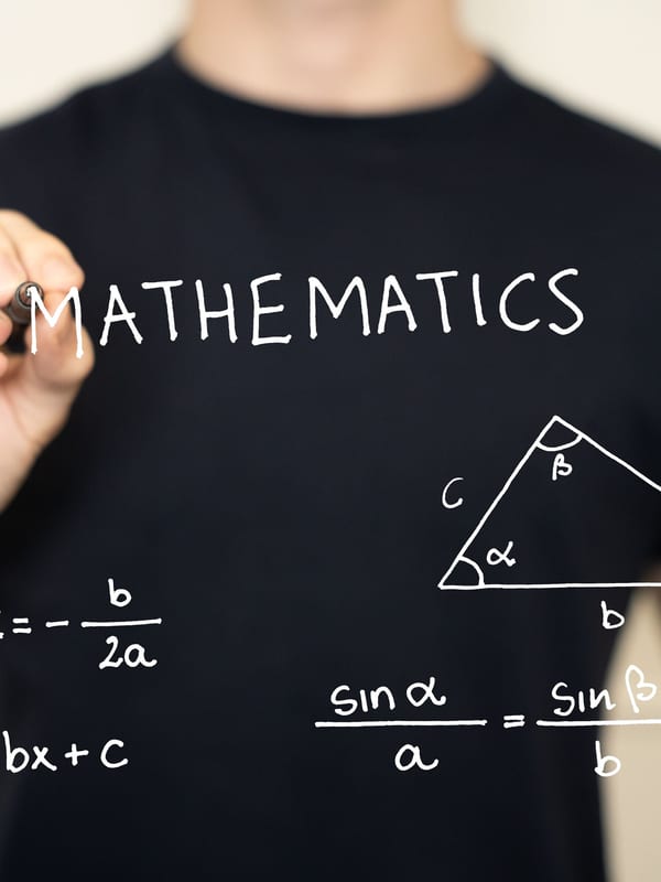 A hand writing the sine rule and quadratic formula on a clear board